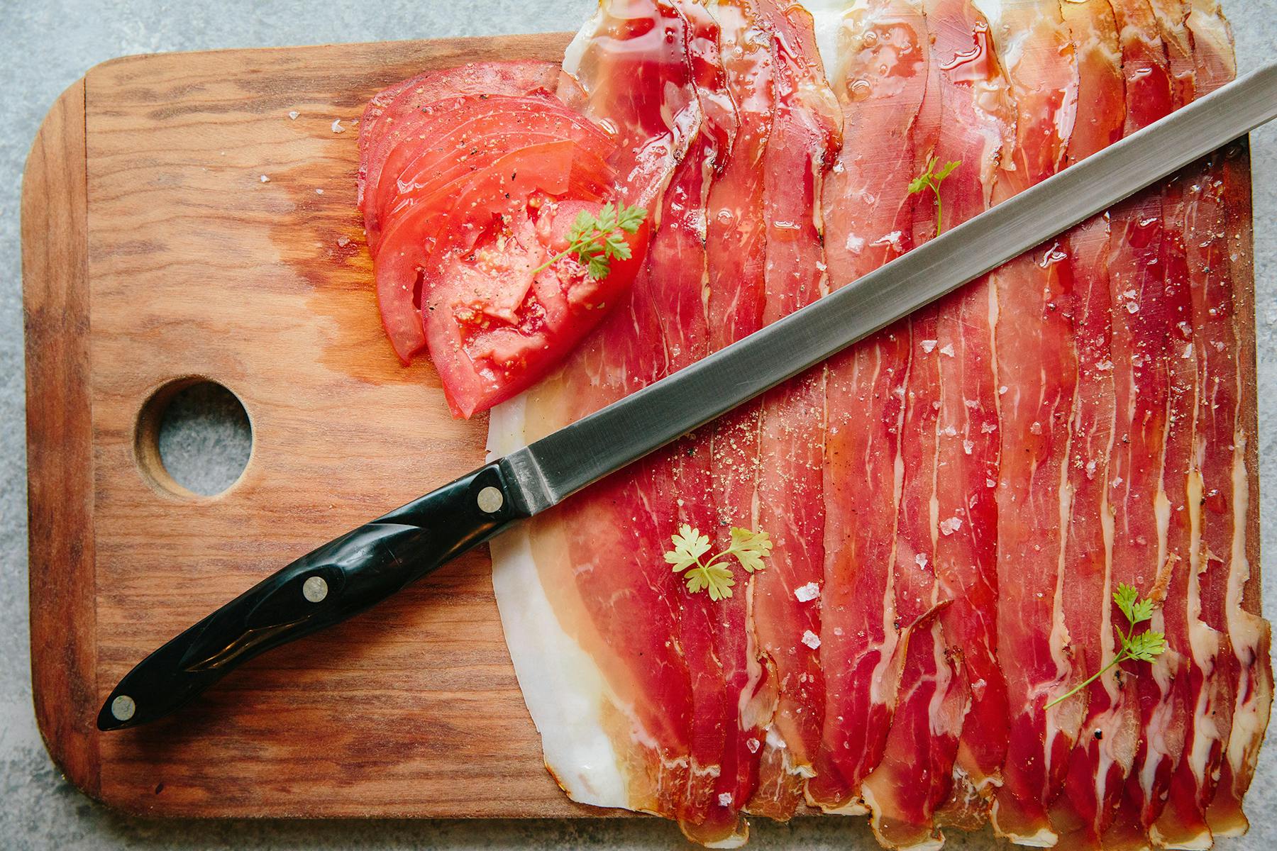 a cutting board with ham and a knife on top